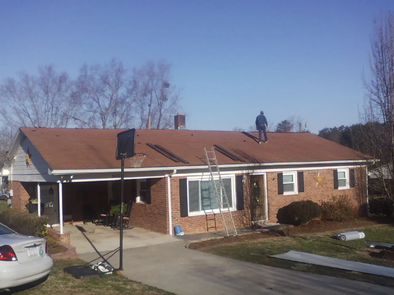Roofer stripping a shingle roof on a brick ranch before metal panels in Port Washington