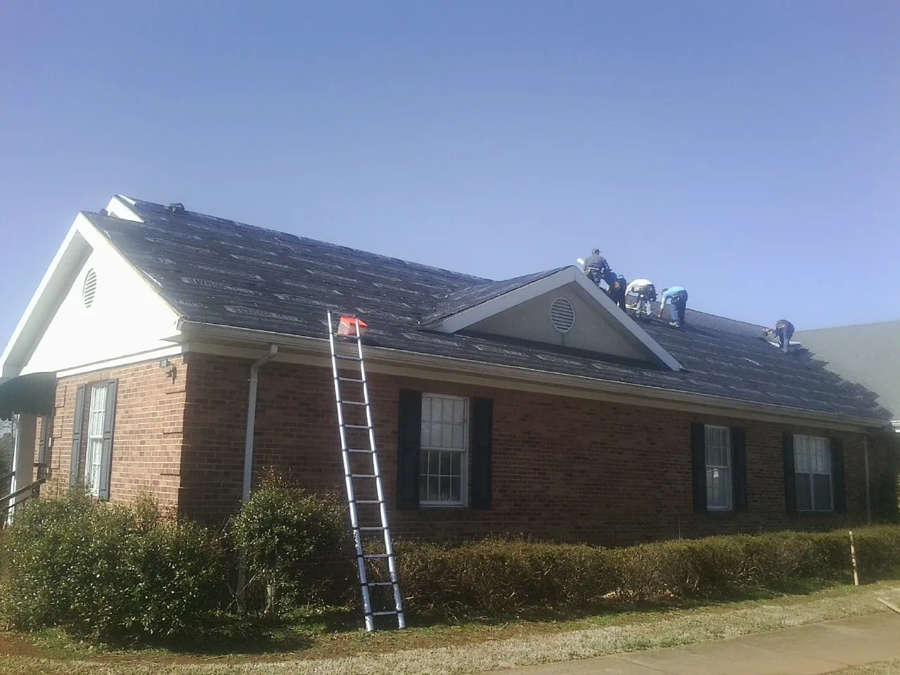 Crew tearing shingles off a brick ranch roof with a ladder set — Metal Roof Repair work by our crew in Port Washington