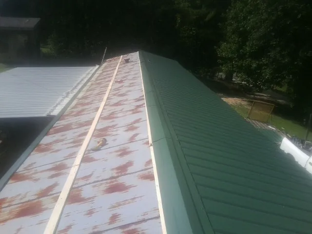 Old rusted panels beside newly installed green metal roofing — Wind Damage Roof Repair by Roofing Brothers in Port Washington