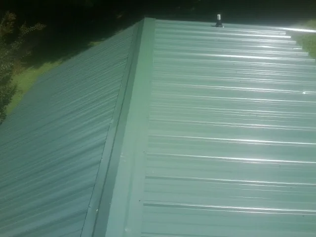 New green metal panels meeting at the ridge of a roof — Flat Roof Repair work by our crew in Port Washington