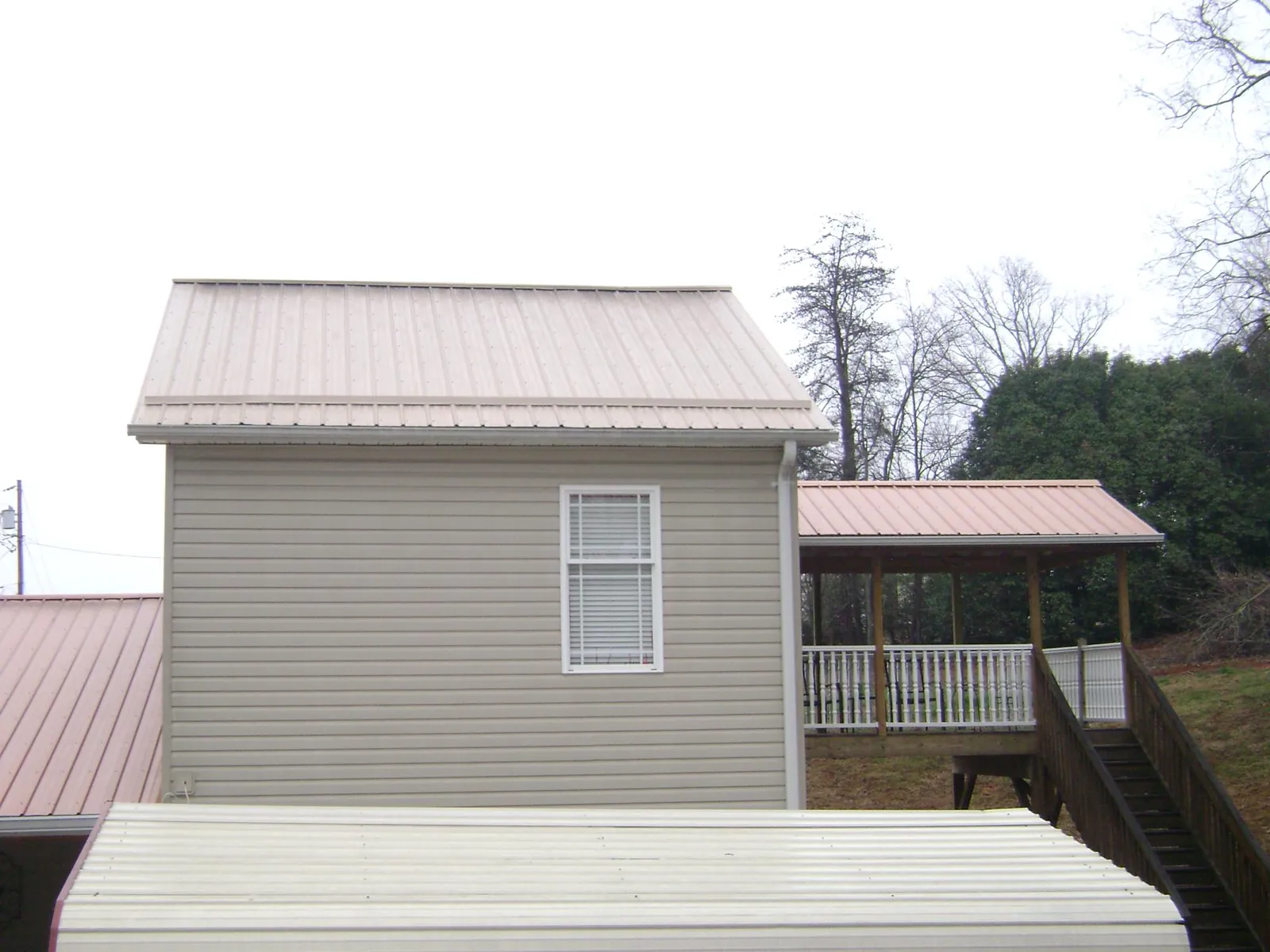 Tan metal roofs on a two story addition and attached porch, from a Roof Replacement job in Port Washington